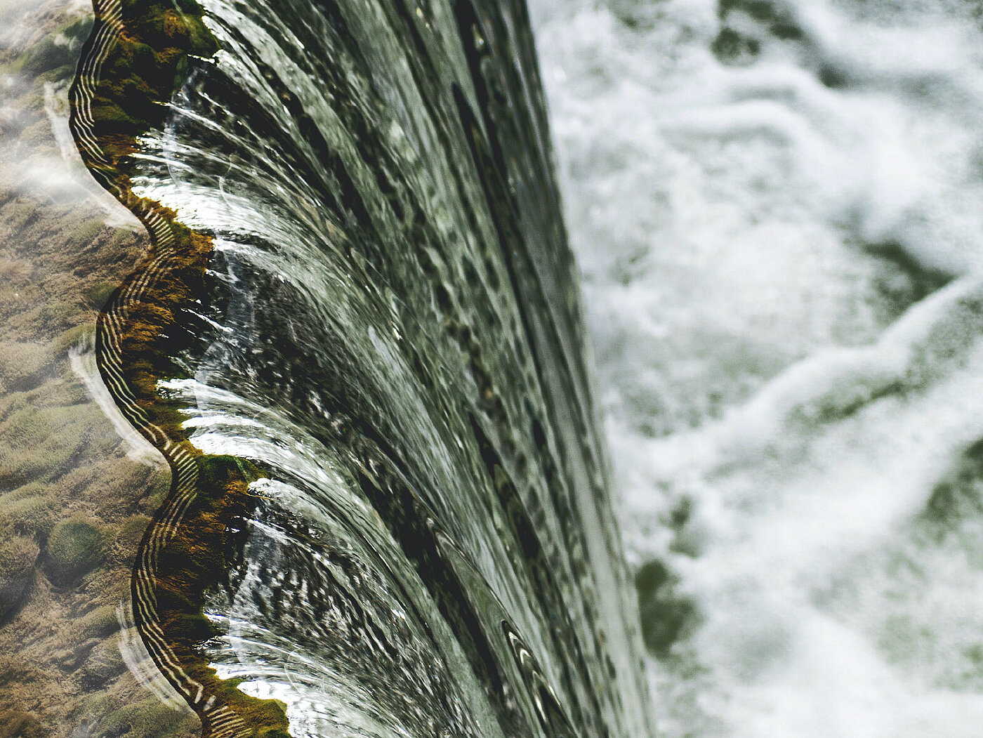 Bildausschnitt eines großen Wasserfalls. Das Wasser eines Flusses fällt aus großer Höhe in die Tiefe.